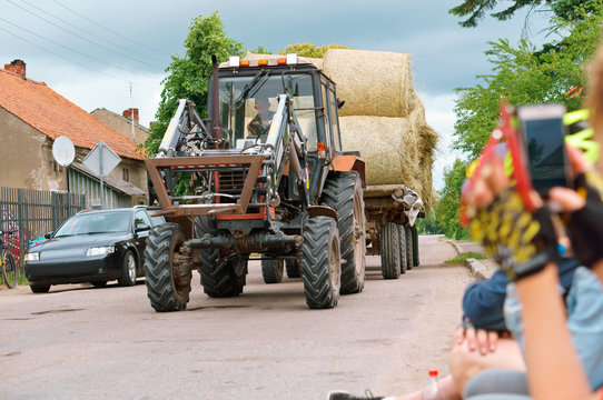 The tractor transports twisted sheaf hay. Straw rolls in the trailer of the agricultural machine.