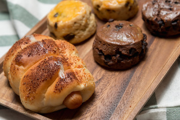 closeup delicious sausage bread roll and fresh tasty scones on wooden table