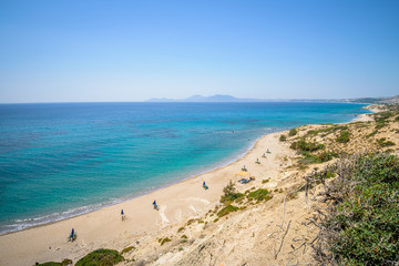 Fototapeta na wymiar Beaches, Greece, Kos Island, Cap Helona: beautiful holiday setting on a secluded beach with umbrellas on the Greek Aegean Sea with turquoise waters and a picturesque bay and islands in the background
