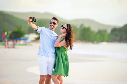 Happy couple taking a photo on white beach on honeymoon holiday