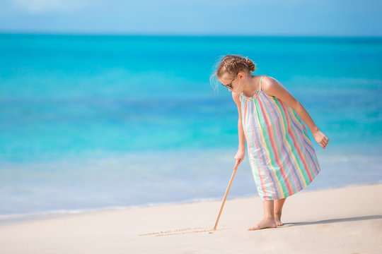 Adorable little girl at beach during summer vacation drawing on sand