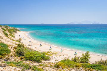 Beaches, Greece, Kos Island, Cap Helona: beautiful holiday setting on a secluded beach with umbrellas on the Greek Aegean Sea with turquoise waters and a picturesque bay and islands in the background - obrazy, fototapety, plakaty
