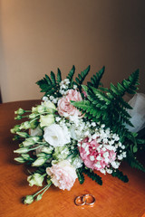A wedding bouquet of roses. Gold rings on the table.