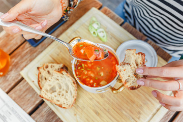 A woman eats a traditional Hungarian goulash or tomato soup from a saucepan in an outdoor restaurant