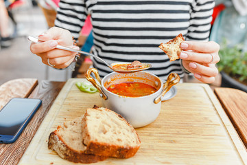 A woman eats a traditional Hungarian goulash or tomato soup from a saucepan in an outdoor restaurant - obrazy, fototapety, plakaty
