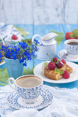 Small cupcakes with berries, strawberries and cherries. Delicious sweet breakfast and fragrant coffee, on a blue wooden background and flowers. Copy space