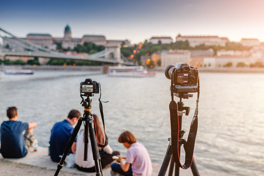 Cameras on tripods photograph a bridge and a river in the city of Budapest. Concept training and Workshop or masterclass on landscape and city photography.