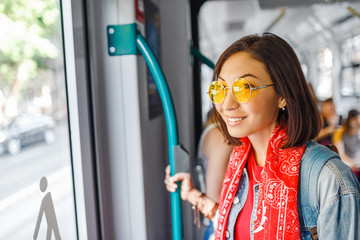 An Asian woman with glasses is sitting in a tram or bus, public transport concept