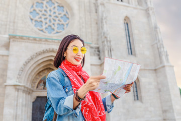 young asian girl tourist studying a map near gothic cathedral at a typical European central square