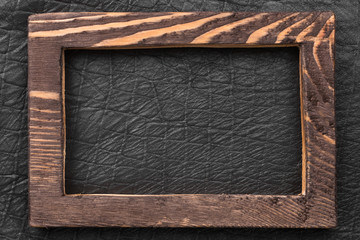 Beautiful wooden frame cut from a solid dark board, lies on a black leather.