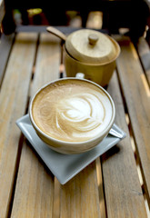 Hot coffee late in design ceramic cup and wooden sugar bowl on wooden table background