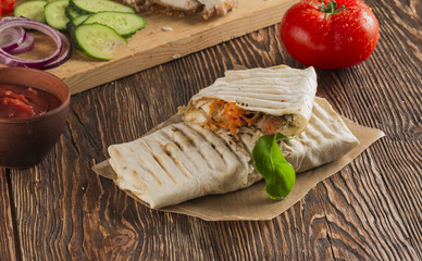 Fototapeta na wymiar Shaurma, cut in half, meat with vegetables in a bread cake, top view on an old wooden rustic background, on a wooden board with tomato and pepper, copy space