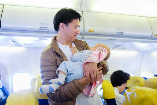 Tenderness. Young Father Is Lulling Asian Cute Baby Boy During Flight On Commercial Airplane. Concept Photo Of Air Travel With Baby: Shallow Depth Of Field