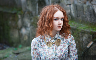 Portrait of a young red-haired curly girl with freckles in a vintage necklace