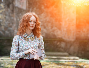 young red-haired curly-haired girl with freckles posing in a summer garden with a vintage book in her hands