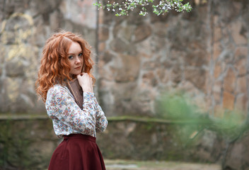 Young red-haired curly-haired girl with freckles posing in a summer garden with a vintage book in her breast