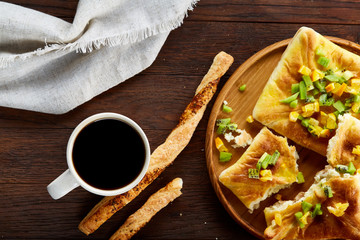 Morning concept with a cup of coffee, breadsticks, fruit pies and oranges on wooden background.