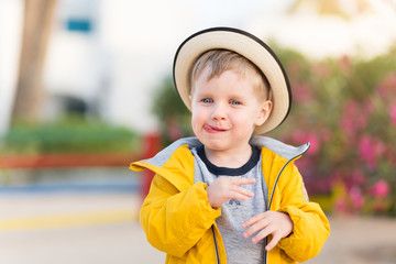 Little smiling kid boy show his tongue out and laughs. Portrait of 3 years old child in straw hat put out one's tongue on summer outdoors