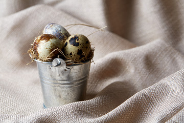 Small decorative bucket filled with quail eggs on napkin over white textured background, close-up, selective focus.