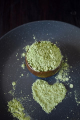 Green matcha tea powder forming a heart on a dark plate