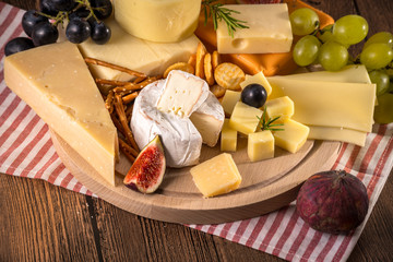 Assorted cheeses on round wooden board plate Camembert cheese, cheese grated bark of oak, hard...