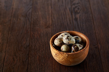 Fresh quail eggs in a wooden bowl on a dark wooden background, top view, close-up