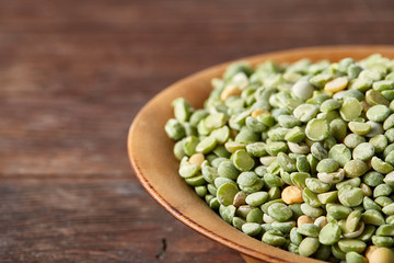 Raw green peas on a wooden plate over rustic background, close-up, selective focus, shallow depth of field.