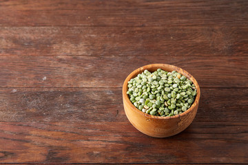 Raw green peas on a wooden plate over rustic background, close-up, selective focus, shallow depth of field.