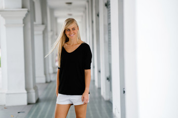 An image of a pretty and young blonde woman standing in the corridor of an old colonial style building. She is an exchange student and enjoys wandering around her new campus.