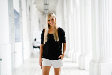 Obraz premium Portrait of a young and charming blonde woman with blue eyes. She is wearing a black shirt and white shorts.
