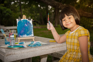 Cute  girl painting on the easel in the garden and having fun