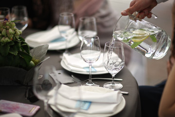 The waiter pours water with lemon and mint into glasses on a serving table - 209479275