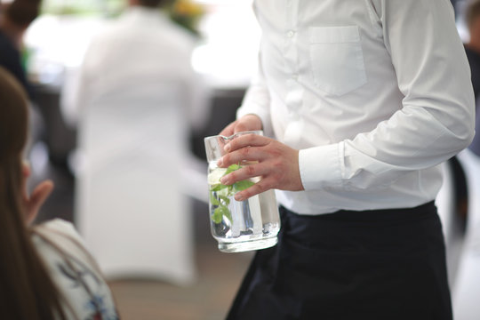 The waiter is holding a jug with a soft drink with fresh mint