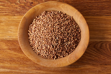 Bowl full of buckwheat grains on rustic wooden table, close-up, selective focus, shallow depth of field.