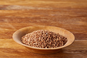 Bowl full of buckwheat grains on rustic wooden table, close-up, selective focus, shallow depth of field.