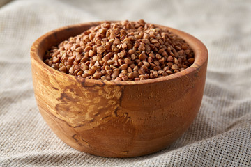 Bowl full of buckwheat grains on rustic wooden table, close-up, selective focus, shallow depth of field.