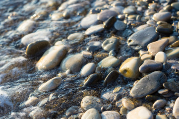 pebble stones on the sea beach, the rolling waves of the sea with foam