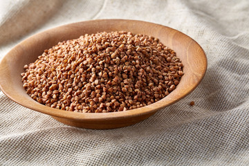 Bowl full of buckwheat grains on rustic wooden table, close-up, selective focus, shallow depth of field.