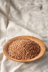Bowl full of buckwheat grains on rustic wooden table, close-up, selective focus, shallow depth of field.