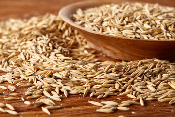 Pile of unpeeled oat grains on wooden background, top view, close-up, macro, shallow depth of field.