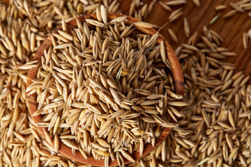 Pile of unpeeled oat grains on wooden background, top view, close-up, macro, shallow depth of field.