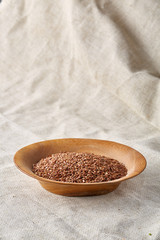 Bowl full of buckwheat grains on rustic wooden table, close-up, selective focus, shallow depth of field.