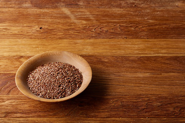Bowl full of buckwheat grains on rustic wooden table, close-up, selective focus, shallow depth of field.