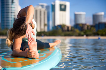 Athletic young woman in SUP Yoga practice side bend Pose in Ala Moana Hawaii
