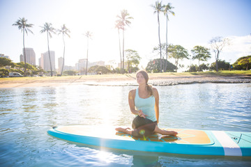 Sunny morning sun flare moment of a pretty young woman in SUP Yoga practice in twist pose