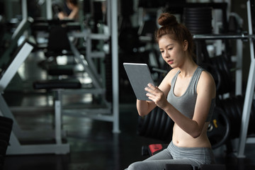 Young sport woman relaxing by using tablet in the gym after exercise.