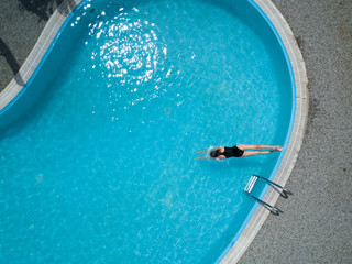 Fototapeta na wymiar Birds eye view, young girl in black swimsuit, jumps into a swimming pool.