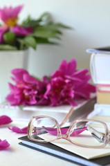 Obraz na płótnie Canvas Bold violet pink peonies with blush pink glasses on a desk. Elegant feminine styled desktop workspace.Concept of working from home office and studying.