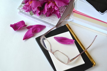 Bold violet pink peonies with blush pink glasses on a desk. Elegant feminine styled desktop workspace.Concept of working from home office and studying.


