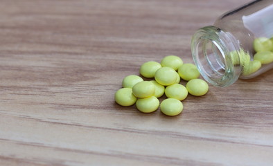 Yellow tablets and glass bottle on a wooden background